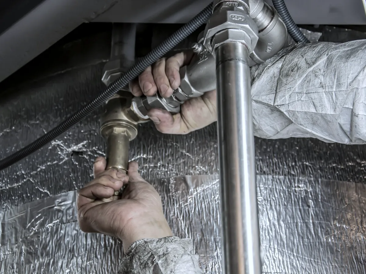 A plumber's hands tightening brass supply fittings beneath a fixture