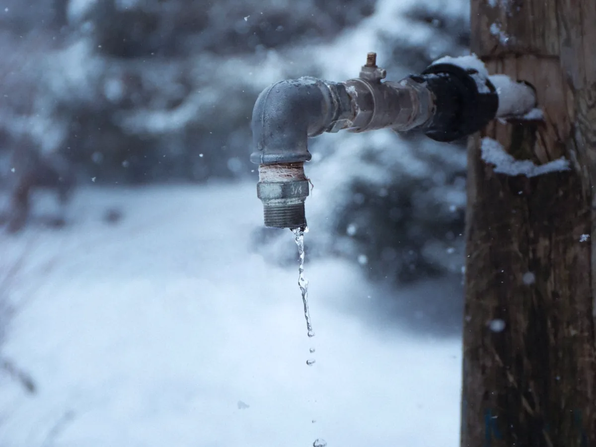 An outdoor spigot left dripping during a hard freeze, snow falling behind it