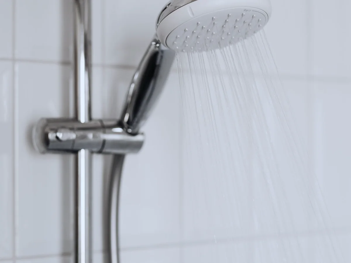 A chrome shower head running water against white tile