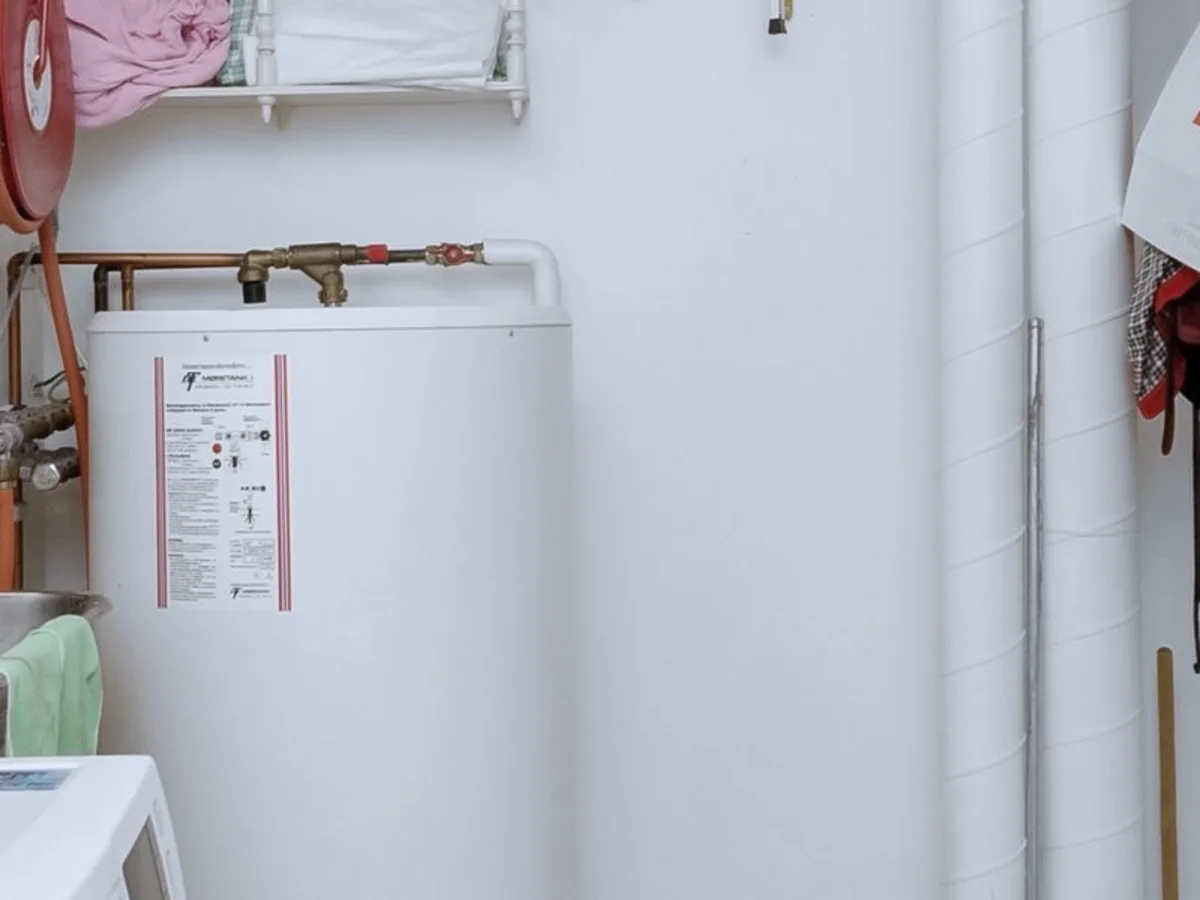 A storage water heater tank in a utility room with copper supply lines above it